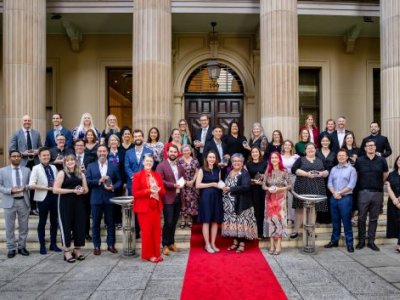 A group of UQ researchers holding award trophies standing out the front of a sandstone building on a red carpet